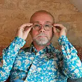 Portrait d'un psychologue clinicien, barbu et portant des lunettes, les ajustant, avec un regard attentif et engageant, symbolisant l'écoute et l'expertise.